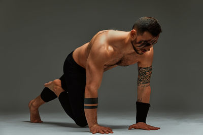 Low section of shirtless man exercising against gray background