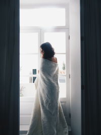 Rear view of woman with wrapped in blanket standing at home