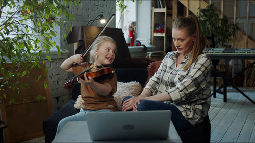 Daughter playing violin while sitting with mother at home