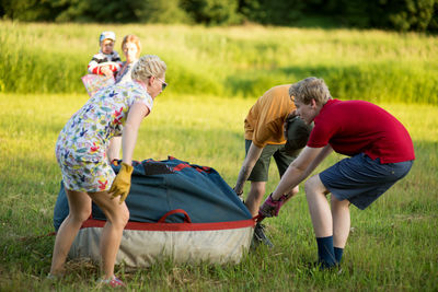 Boys assisting female pilot in preparing hot air balloon on grassy field during sunset