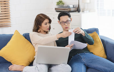 Young woman using smart phone while sitting in laptop