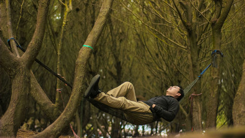 Young man climbing on tree trunk in forest