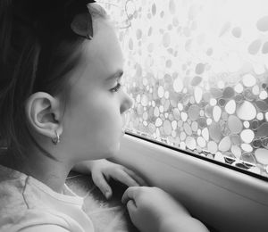 Side view of girl looking through window at home