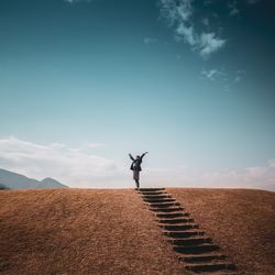 Full length of young woman with arms raised standing on land against sky