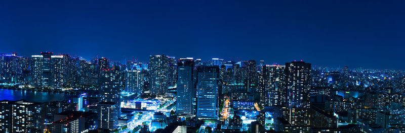 Illuminated cityscape against clear blue sky at night
