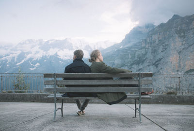 Rear view of people sitting on bench against mountains