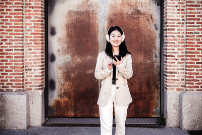 Happy business woman listening to music on headphones and mobile phone in city