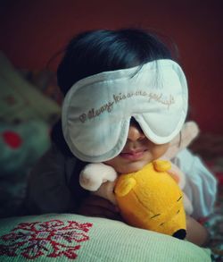 Close-up of cute girl wearing sleep mask holding stuffed toy on bed at home