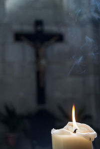 Close-up of lit candle against cross