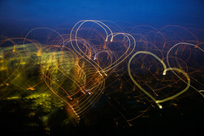 Close-up of heart shapes light trails against sky at night