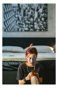 Young woman using smart phone while sitting against bed