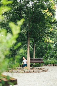 Boy sitting by tree against plants