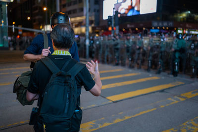 Rear view of man holding umbrella on road at night