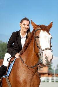 Portrait of young woman riding horse against sky
