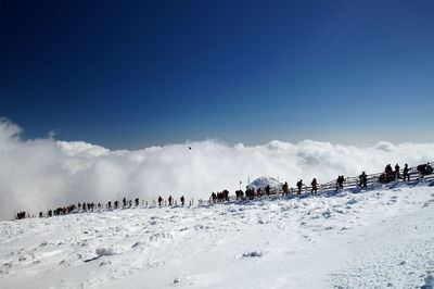 People on snow covered landscape against blue sky