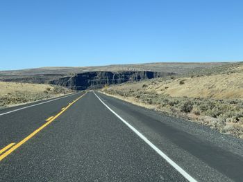 Road leading towards mountain against clear sky