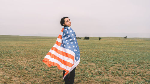 Smiling young woman standing on field against sky