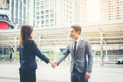 Smiling colleagues handshaking while standing against buildings in city