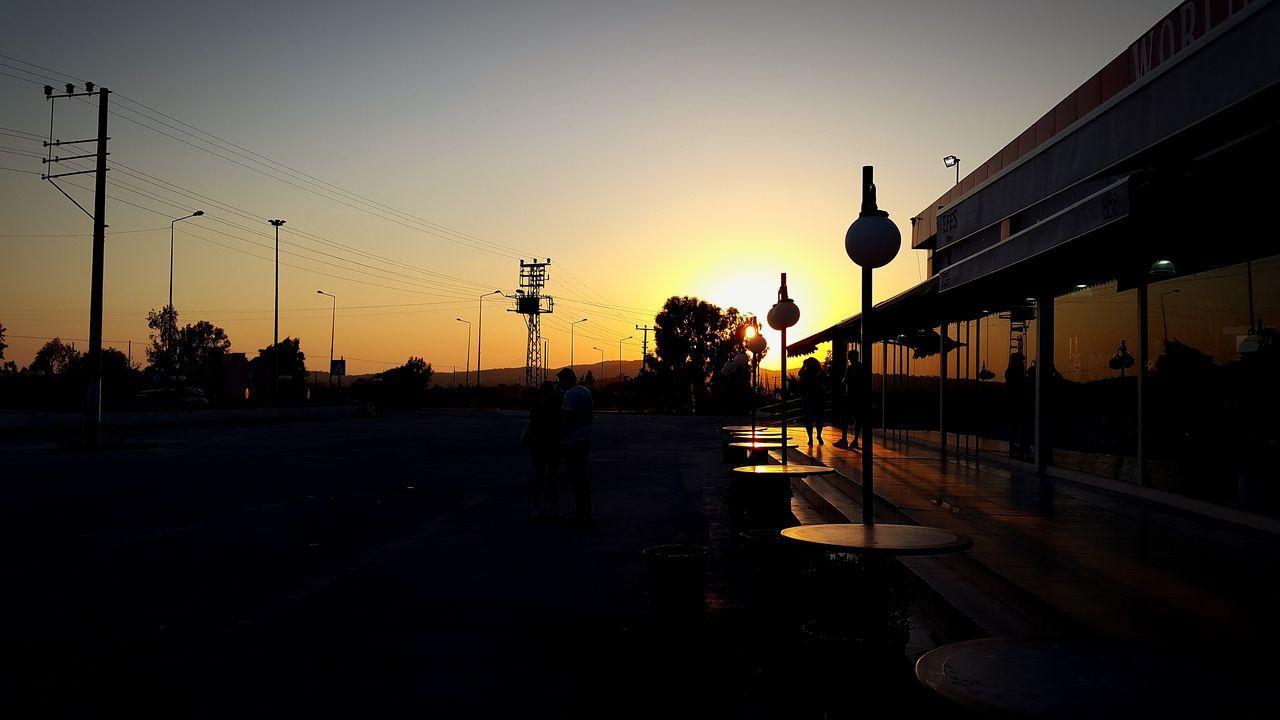 sunset, clear sky, silhouette, street light, transportation, men, street, sky, lifestyles, orange color, road, building exterior, copy space, walking, built structure, person, sun, sunlight