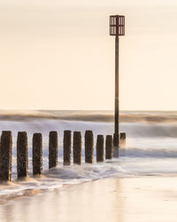 Wooden post in sea against sky during sunset