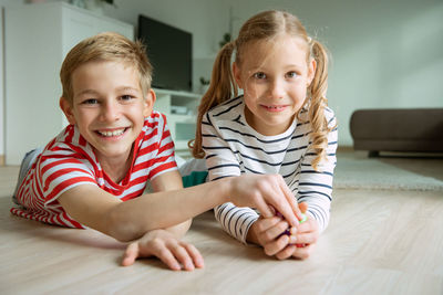 Portrait cheerful siblings playing with dice while lying on carpet at home