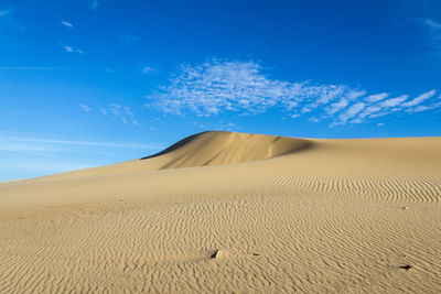 Sand dunes in desert against blue sky