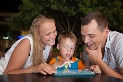 Happy parents looking at son using digital tablet on table in cafe