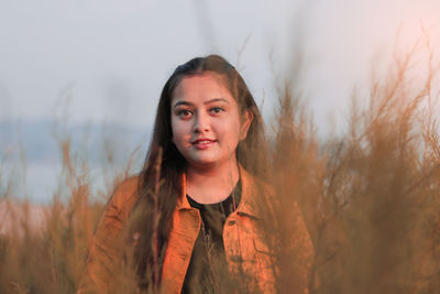 Portrait of smiling young woman standing on land against sky