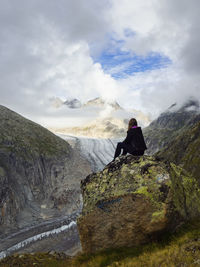 Woman sitting on rock against cloudy sky