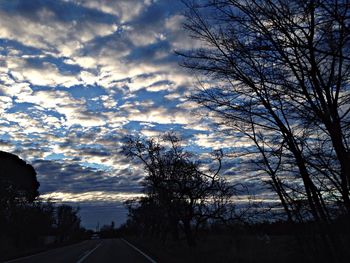 Road passing through forest against cloudy sky