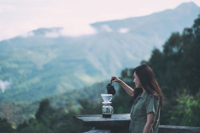 Woman making coffee on railing against mountains