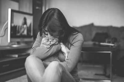 Side view of woman holding cat while sitting at home