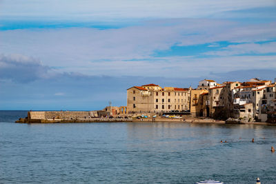 Buildings by sea against cloudy sky