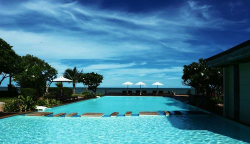 Swimming pool by trees against blue sky