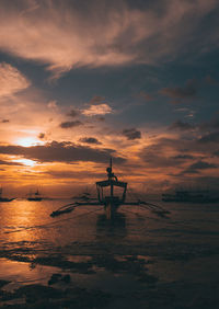 Outrigger boat in sea against sky during sunset