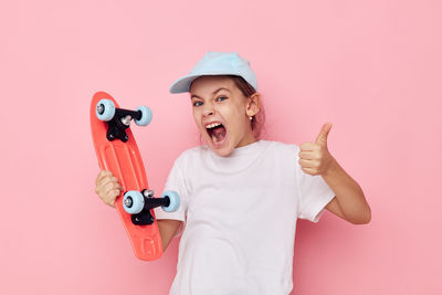 Portrait of cheerful girl holding skateboard against pink background