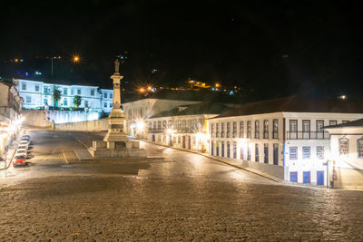 Illuminated street by buildings in city at night