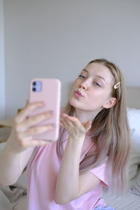 Cute girl 15-18 years old sitting on the bed makes a selfie.