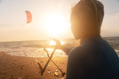 Rear view of woman standing at beach against sky during sunset