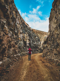 Rear view of woman standing on rock against sky