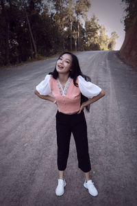 Portrait of young woman standing on road against trees