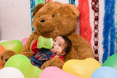 Baby girl by balloons and teddy bear at home