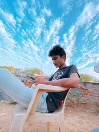 Young man sitting on seat against sky