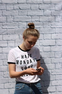 Teenage girl using mobile phone while standing against brick wall