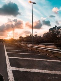 Road by railroad tracks against sky during sunset