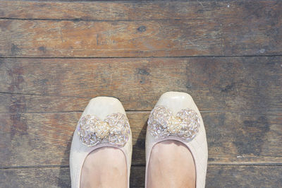 Low section of woman wearing shoes standing on wooden floorboard