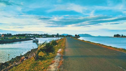 View of road by river against cloudy sky