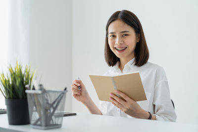 Portrait of smiling businesswoman holding diary while sitting at desk in office