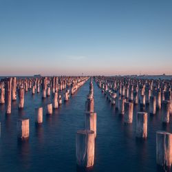 Wooden posts in row on lake against sky