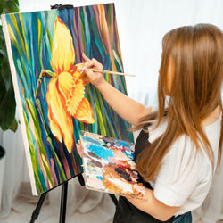 Side view of woman with long hair painting on canvas